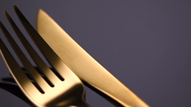 Luxury golden cutlery closeup. Knife and fork over black background. Rotation 360 degrees. 4K UHD video