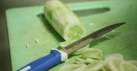 fresh cutting cucumber with knife at table.