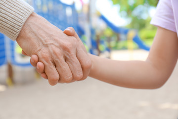 Senior woman and little child holding hands, closeup