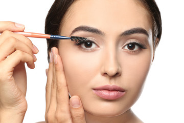 Beautiful young woman with eyelash extensions applying mascara, on white background