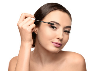 Beautiful young woman with eyelash extensions applying mascara, on white background