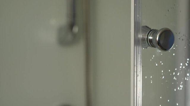 Hand on a door handle of a glass shower cabin in order to open or close it. Shower bulkhead Handle close-up