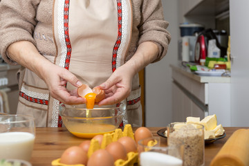 Oma zerschlägt ein Ei. Das Eigelb fließt in eine Glasschale. Sie backt Weihnachtskekse für ihre Enkel