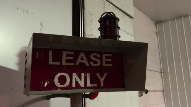 A night view of a flashing "lease only" warning sign outside of a city parking garage.  	