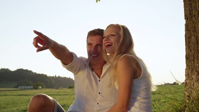 SLOW MOTION CLOSE UP: Young beautiful couple in love talking and kissing in a sunny meadow. Boy and girl enjoying their romantic date in the countryside. Newlyweds gaze at each other sharing a kiss.
