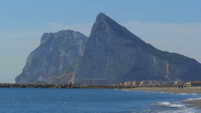 View of the Rock of Gibraltar and the beach with sea waves. Coast of the sea on the border of Gibraltar between Spain and England. Clear blue sky, sunny day in Spain.