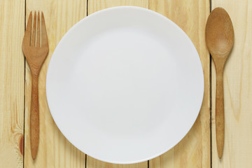 White plate and wooden spoon rests on a brown wood floor.