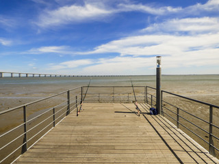 Obraz premium Fishing rods at a pier by the Tagus river at Parque das Nacoes - Vasco da Gama bridge in the background (Lisbon, Portugal)