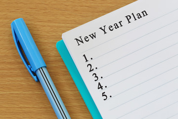 Notebook and pen placed on wood desk and New year plan text.