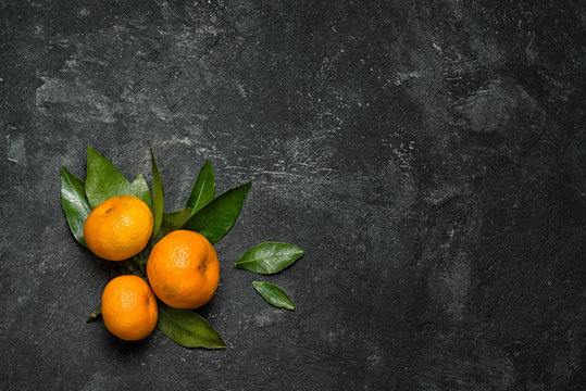 group of three mandarines with leaves on a black cement background with copy space for your menu text