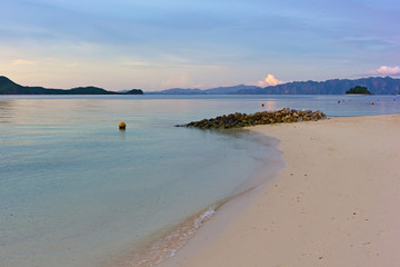Tropical island paradise, Coron Island, Palawan Province, Philippines. Tranquil lagoon landscape with sandy beach and mountains backdrop on horizon at sunrise.