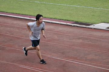 Obraz premium Handsome athlete Asian man running on racetrack in stadium with copy space background. Healthy active lifestyle concept.
