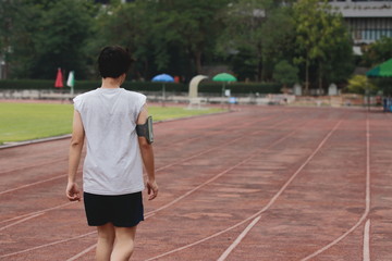 Obraz premium Back view of young Asian walking on racetrack at athletics stadium. Vintage toned image.