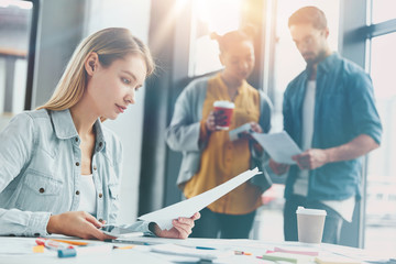 Obraz premium Portrait of skilled web designers meet together, explain new information for making drawing. Serious female model studies document attentively while two colleagues stand in background, have discussion