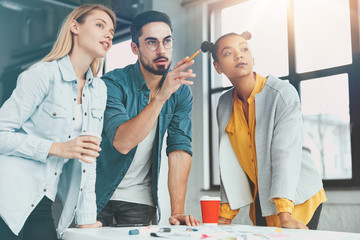 Obraz premium Indoor shot of multiethnic people meet together, look presentation on white board. Skilled young male worker indiactes at multimedia, present financial report, makes workshop or training lesson