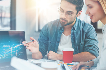 Professional bearded male manager or enterpreneur demonstrates business report on meeting with partner, draws attention to sales, shows graphics on laptop computer, has confident look into screen
