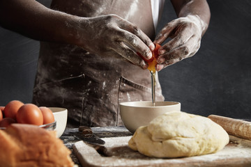 Man`s hands break egg in bowl as prepares pastry. Cropped shot of busy male cook bakes delicious...