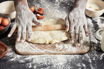 Black man`s hands work with rolling pin, sheet dough on wooden counter, tries new recipe of pastry,...