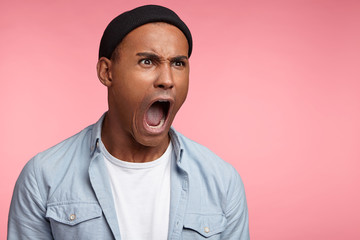 Amazed irritated male boss screams at colleagues, keeps mouth widely opened, dissatisfied with something, yells loudly, expresses negative emotions, isolated over pink background. Mad hipster