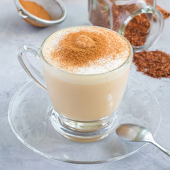 Healthy rooibos red tea latte topped with cinnamon, in a glass cup and ingredients on background, square