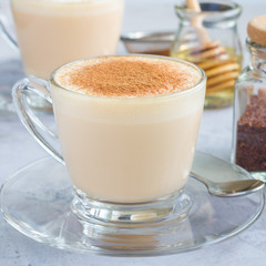 Healthy rooibos red tea latte topped with cinnamon, in glass cup and ingredients on background, square