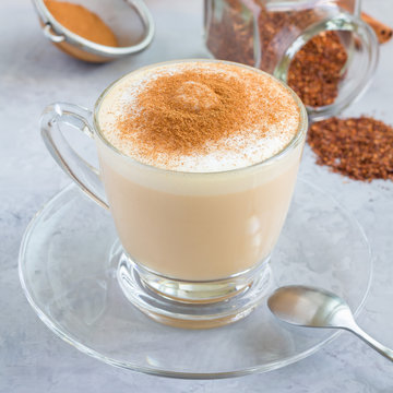 Healthy rooibos red tea latte topped with cinnamon, in a glass cup and ingredients on background, square