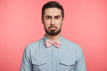 Unhappy gloomy bearded attractive male curves lip has sorrorful expression as recieves refusal from woman to date, feels depressed and lonely, expresses negative emotions. People and emotions concept