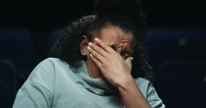 A terrified woman covers her face as she struggles to watch a scary movie at the movie theatre.