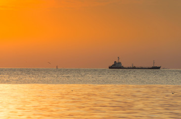 Fototapeta premium The evening sun with beautiful orange light and the cargo ship was running in the sea.