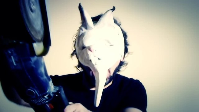 Waving nightmare: an evil man (a crazy maniac, a psycho killer) wearing a scary bunny mask runs towards us with a chainsaw. Comedic horror halloween shot.
