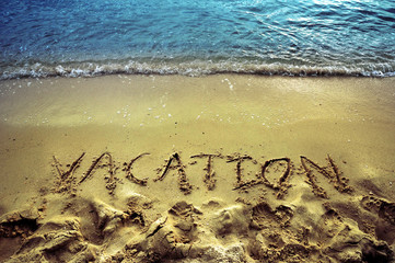 Vacation word spelled on sand beach with blue water