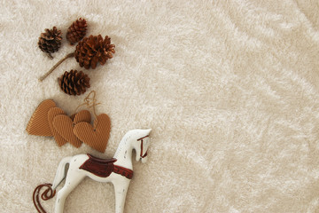 Fototapeta na wymiar pine cones and rocking horse over cozy and fur carpet. Top view.