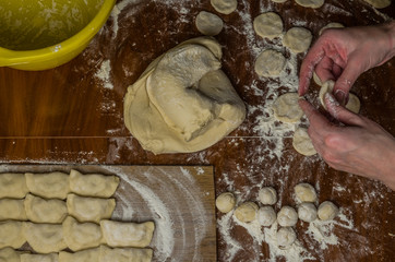 The hands of a woman cook cooked on a table of flour dough and make vareniki