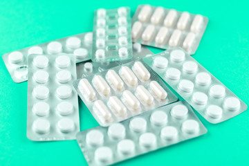 Packs of white capsules and pills packed in blisters with copy space on aquamarine background. Focus on foreground, soft bokeh