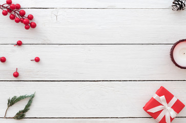 Christmas background with red gift box, holly berry, fir leaves, pine cone and candle on white wooden background. Creative Flat layout and top view design.