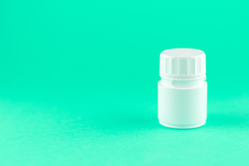 Close up white pill bottle on aquamarine background with copy space. Focus on foreground, soft bokeh. Pharmacy drugstore concept