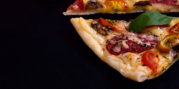 Hot and delicious pizza slices ready to eat on a black wooden background.