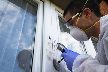 Forensic experts finds fingerprints on the window with the help of a magnifying glass and brushes