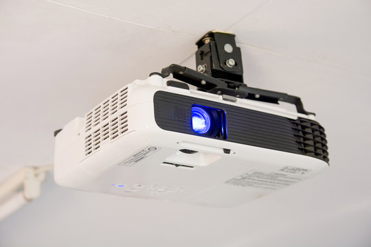 White projector hanging on the ceiling of conference room.