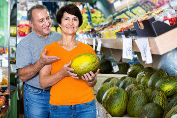 Smiling couple is choosing green melon in the supermarket.