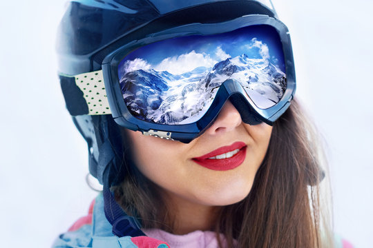 Portrait of young woman at the ski resort on the background of mountains and blue sky.A mountain range reflected in the ski mask