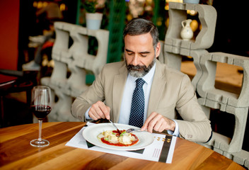 Handsome bearded businessman having lunch and drinking red wine in restaurant