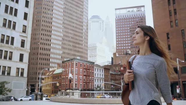 Young beautiful businesswoman holding the documents and walking to work in financial district of New York. Slow motion.