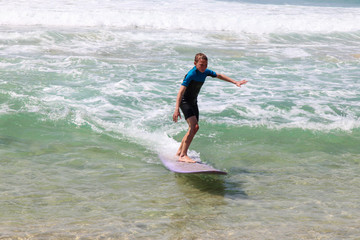 Boy riding wave on purple longboard at the beach.