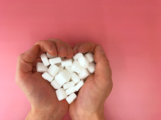 Sugar cubes in hands forming heart shape. Pink soft background. Loving sweet or sugar.