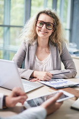 Waist-up portrait of attractive curly manager having project discussion with colleague while gathered together at spacious boardroom