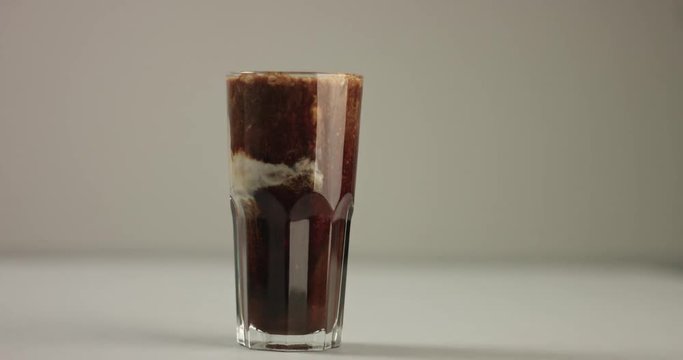Mixing coffee, hot chocolate and steamed milk into a large glass to make a hot drink on light gray background