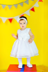 beautiful little girl in white dress is standing on big gift box.