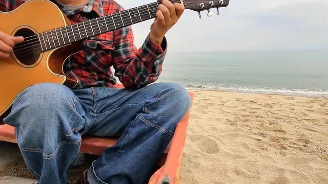Man playing guitar sitting in a boat on the beach