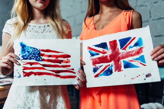 Close-up image of two young women holding a drawing of British and American flags hand-drawn with aquarelle technique on plain paper